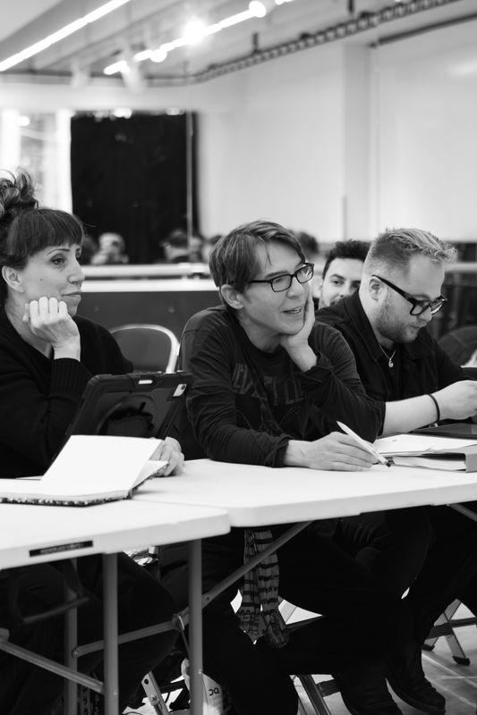 Three people are sat at a table, they look to be taking notes