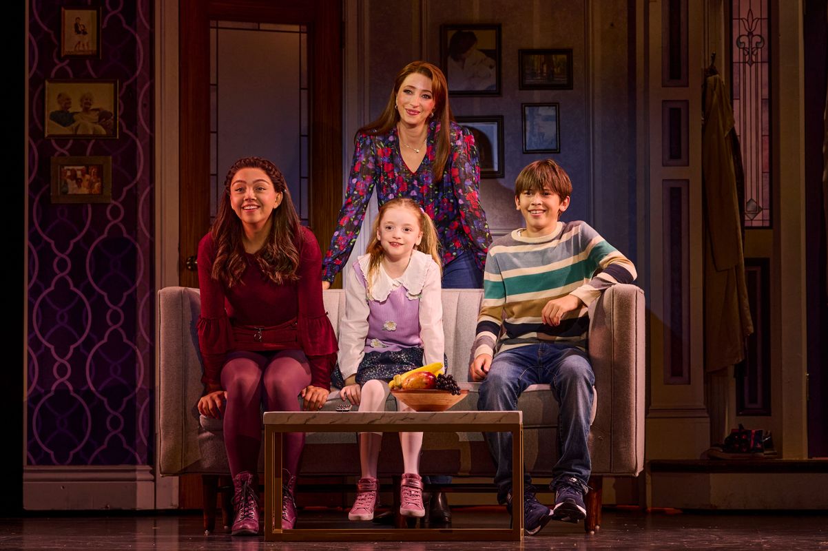Miranda stands behind a sofa with her children sat down infront of her.