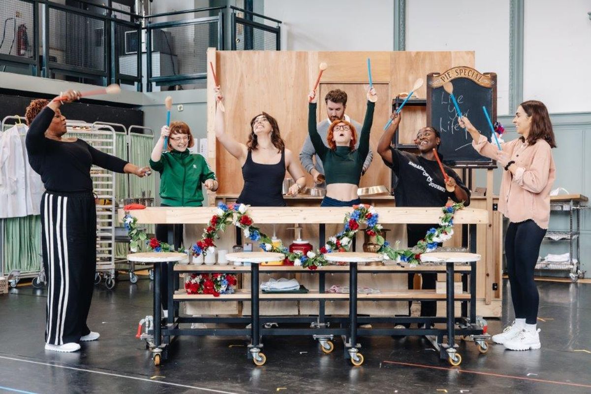 Group of people stood by a long counter on wheels and they are all holding sticks in the air
