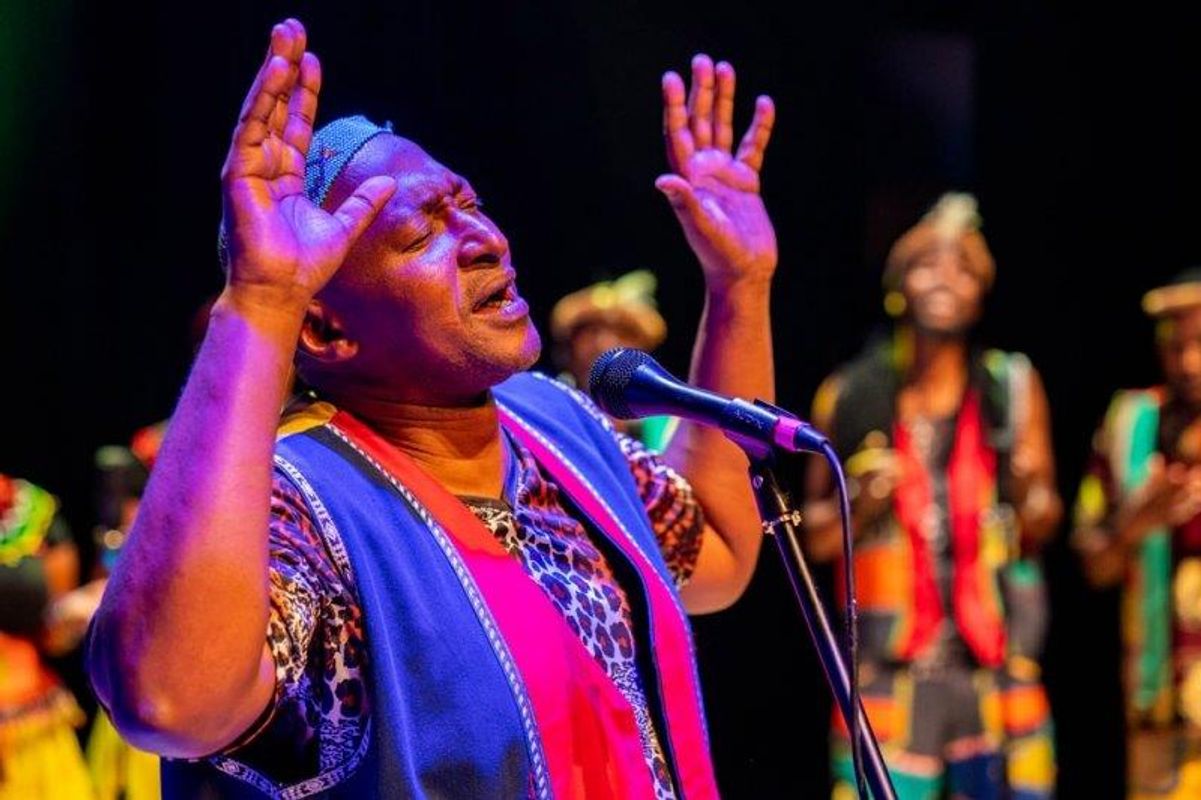The South African Cultural Choir are singing on stage with Paul Simon. They are all wearing bright and vibrant African clothing