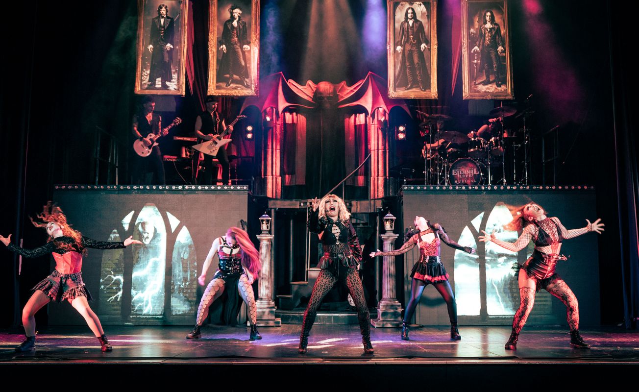 Five people dance on stage waving their arms out at the side.