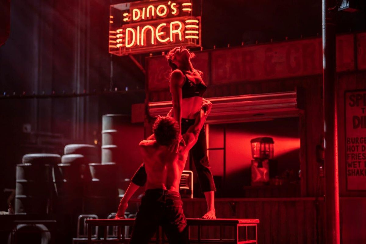 A man and a woman are dancing with each other, there is a red light reflecting onto them creating a tension between them