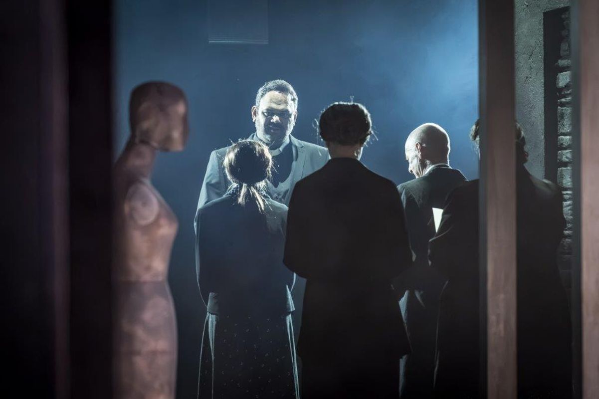 In the foreground there is a mannequin, there are four people with their backs to the viewer and a person stands in front talking to them