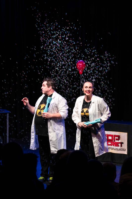 Two people stand on stage wearing lab coats.