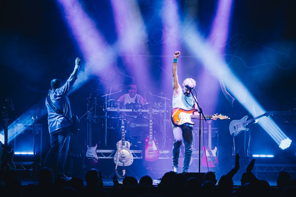 Two people playing guitar raise their fists to the air.