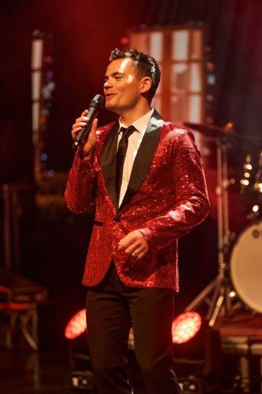A singer stands on stage in a red sequined blazer.