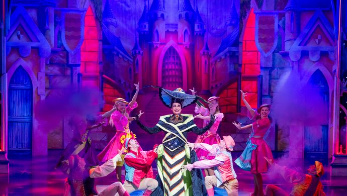 The Wicked Stepmother stands centre stage in a black and yellow dress with a floppy hat.