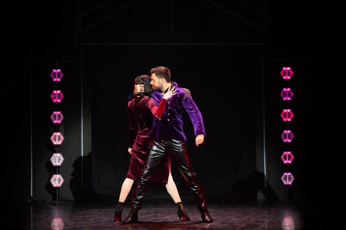 Giovanni and a woman dancer, he is holding her close and her hand is rested on his chest