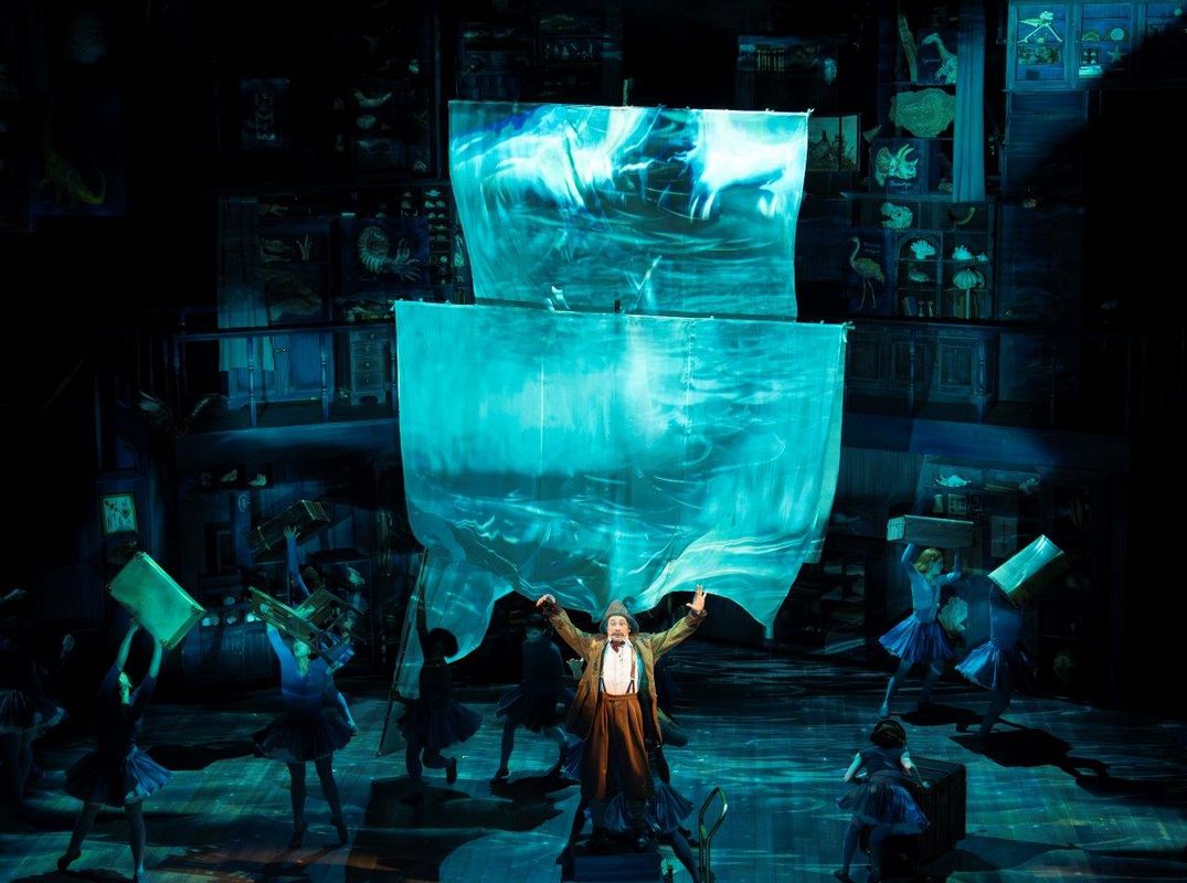 The dancers are performing on what looks like a ship setting. There are big white sales with water projected onto them