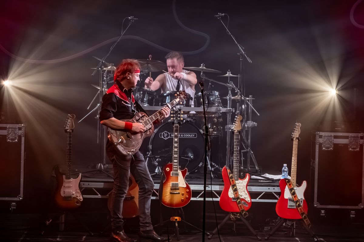 A person plays guitar in front of three other guitars which have been propped up.