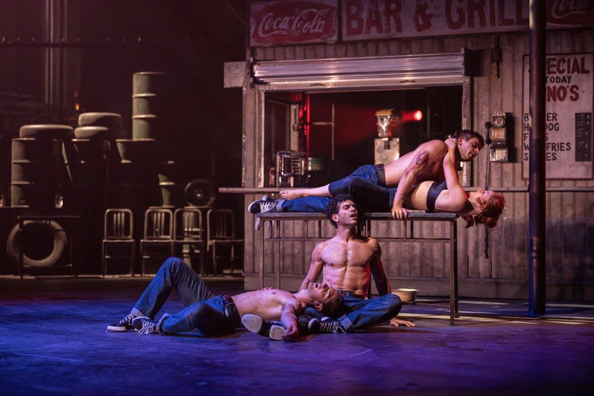 There are three topless men, two of them are on the floor, the other is on top of a woman and they are on a table