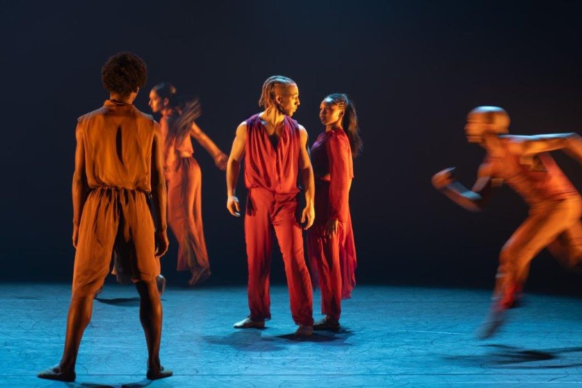 Group of dancers in orange and brown clothing with a soft spot light on them