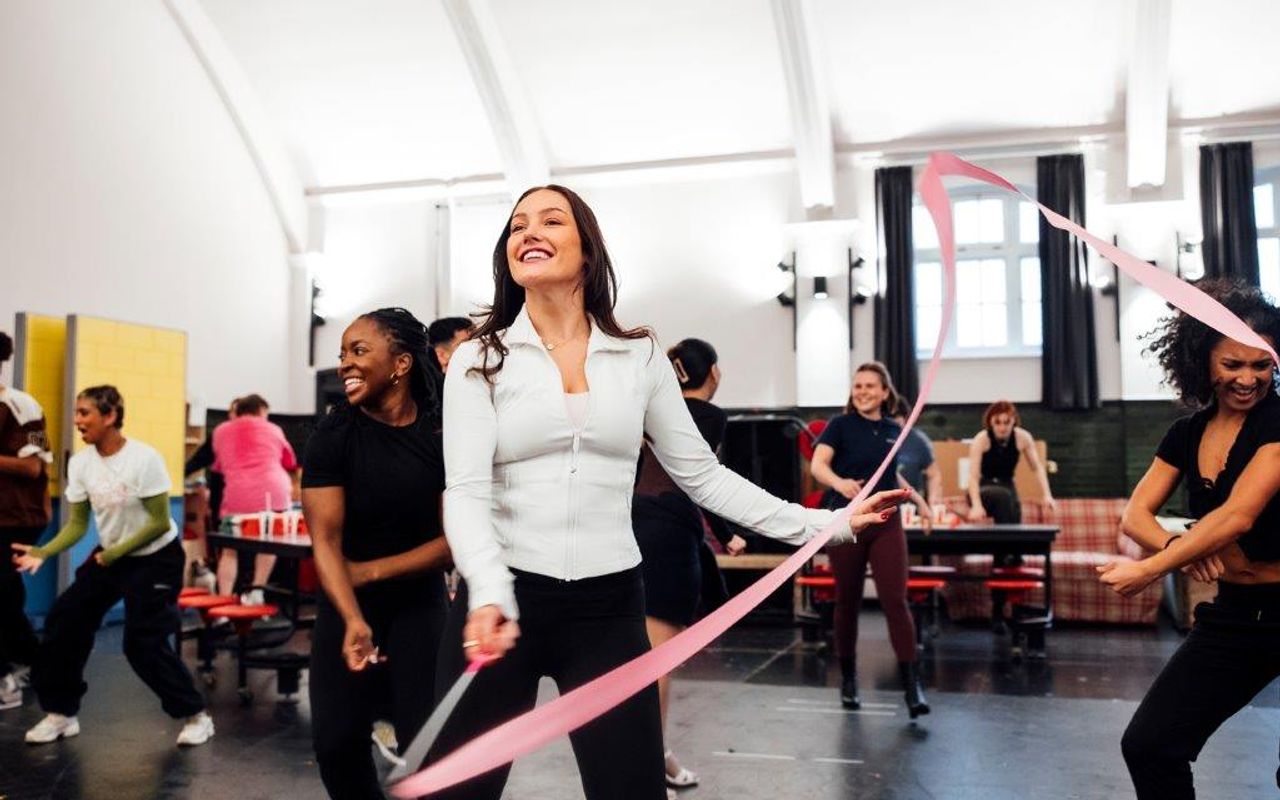 Three people are waving a long pink ribbon on a stick