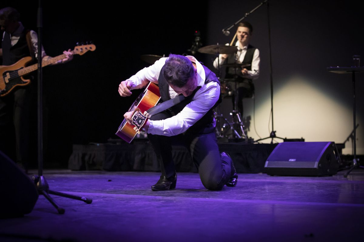 A person in a black waistcoat strums their guitar.