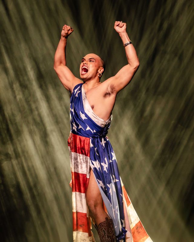 A person draped in an American flag holds their fists in the air.
