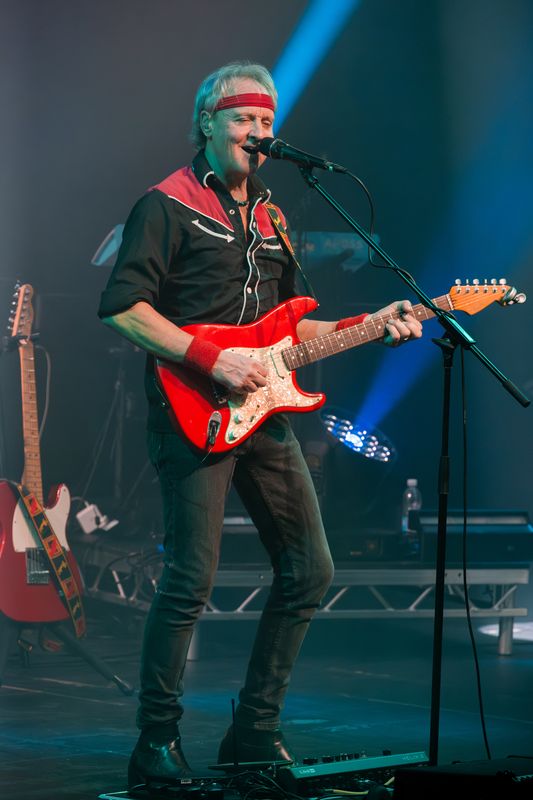 Band on stage performing, they're playing guitars and drums and there are flashing lights around them