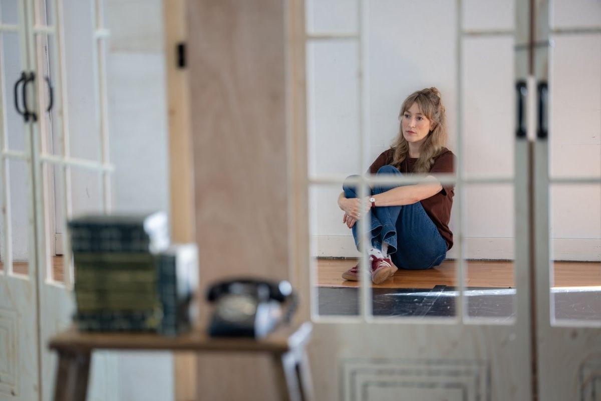 A woman sat on the floor holding her knees to her chest, she looks worried
