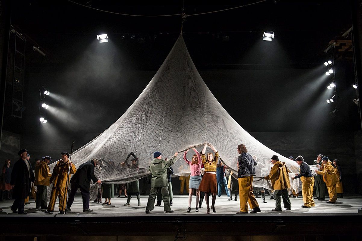 A large group of people hold a gigantic triangle net over their heads.