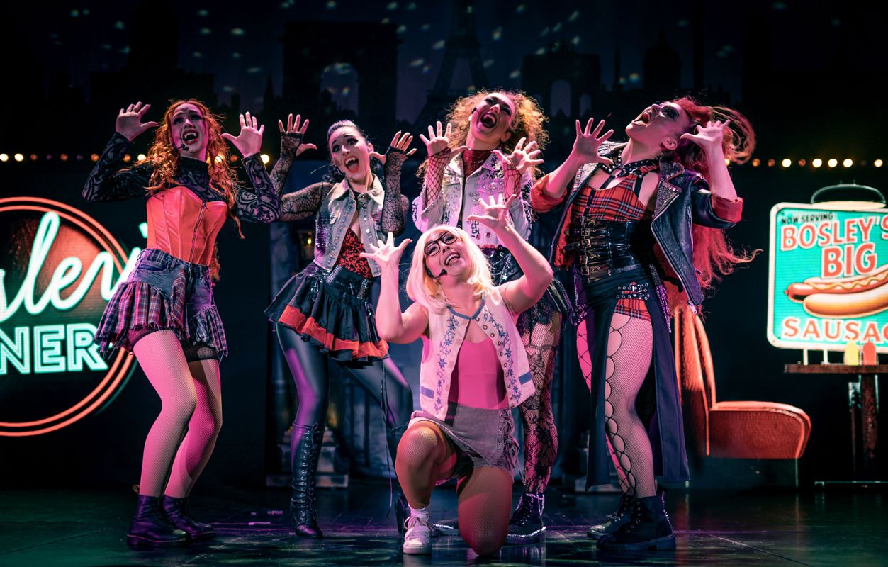 Five people hold both hands up in the air looking surprised.