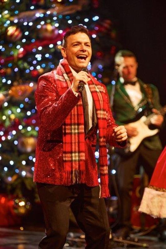 A singer stands on stage in a red sequined blazer and checked scarf.