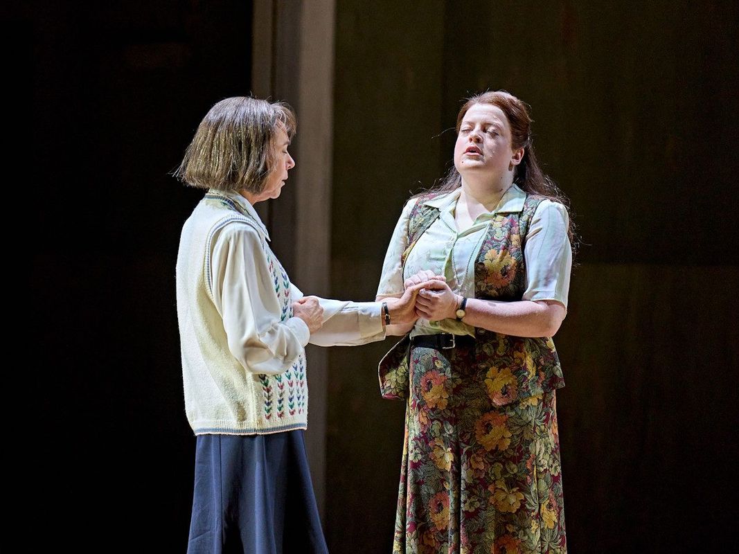 Two women are stood with each other, one is holding onto the other's hand