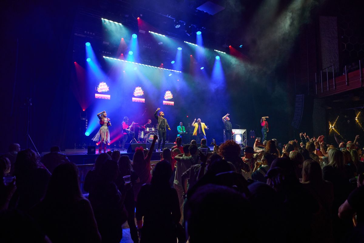 An audience watches five performers jump on stage.