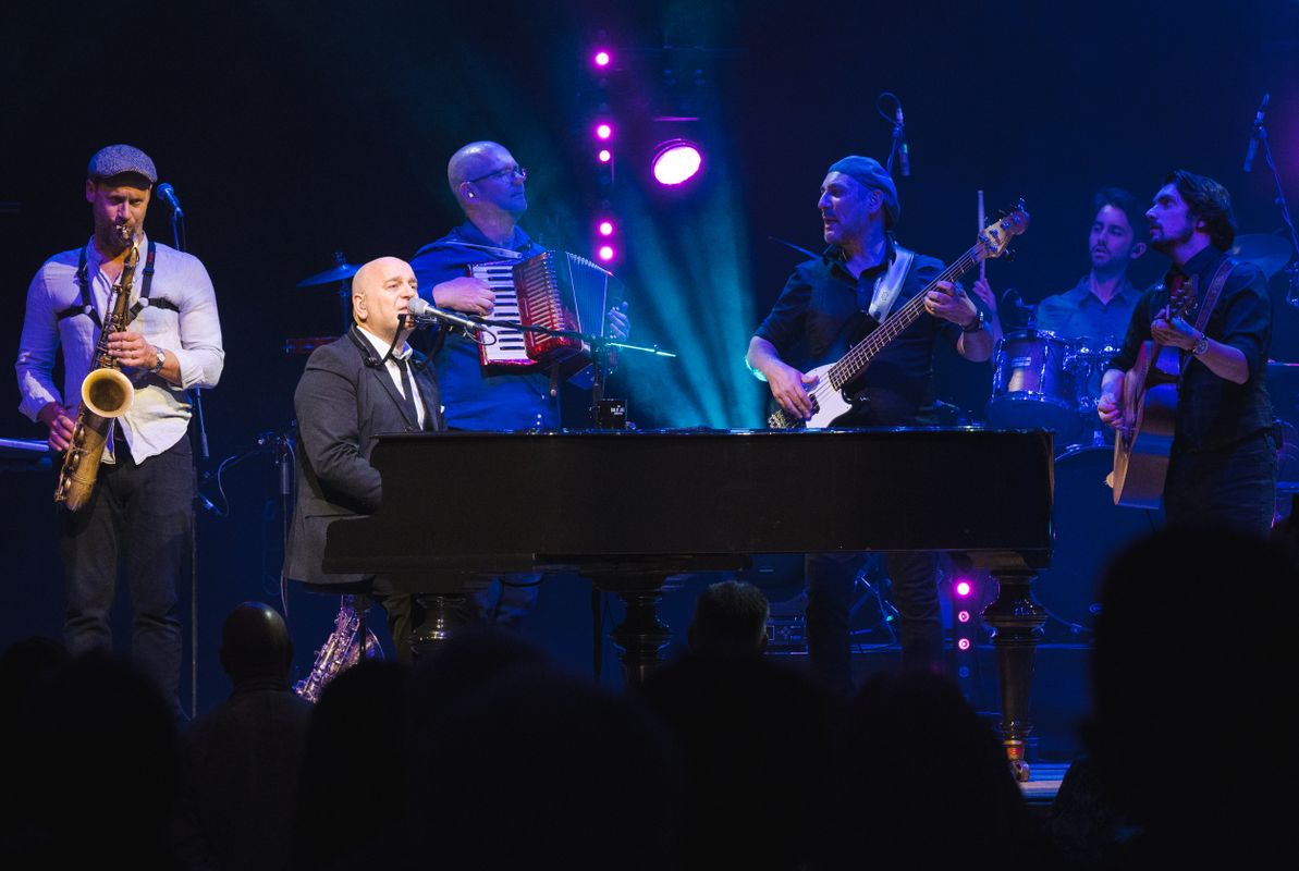 A person plays a black grand piano surrounded by other musicians. 