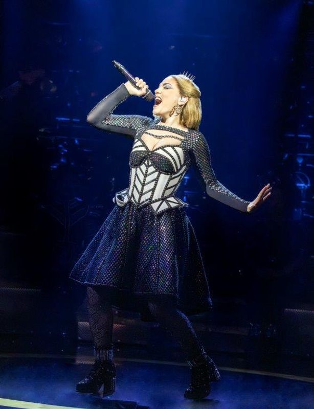 A person in a white and black jewelled outfit  sings on stage.