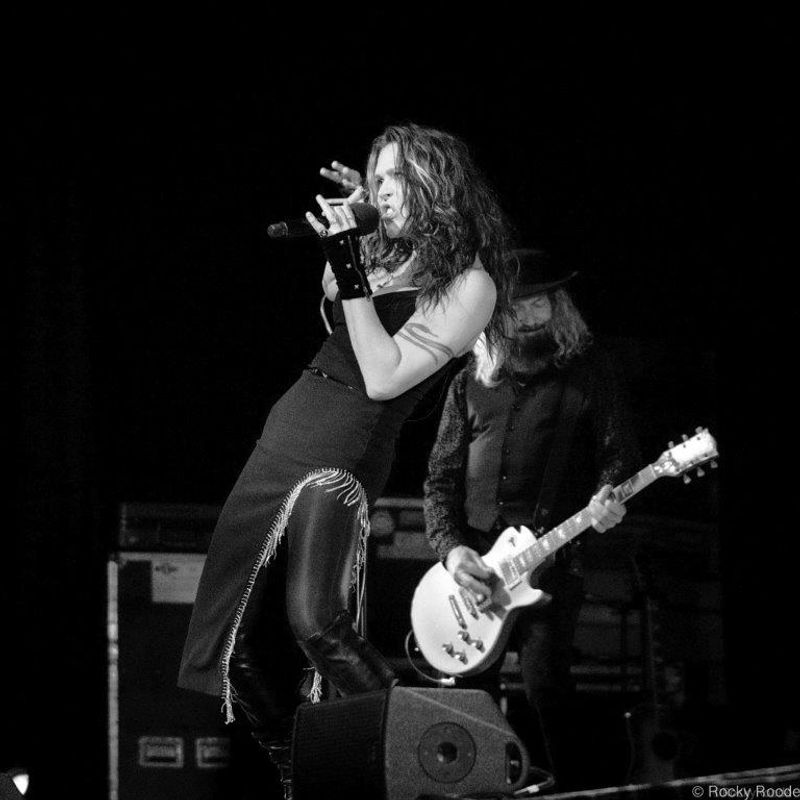 A person sings on stage with a guitarist playing behind.