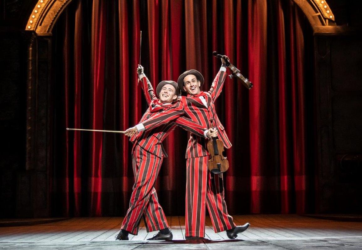 Two men in black and red striped suites holding violins
