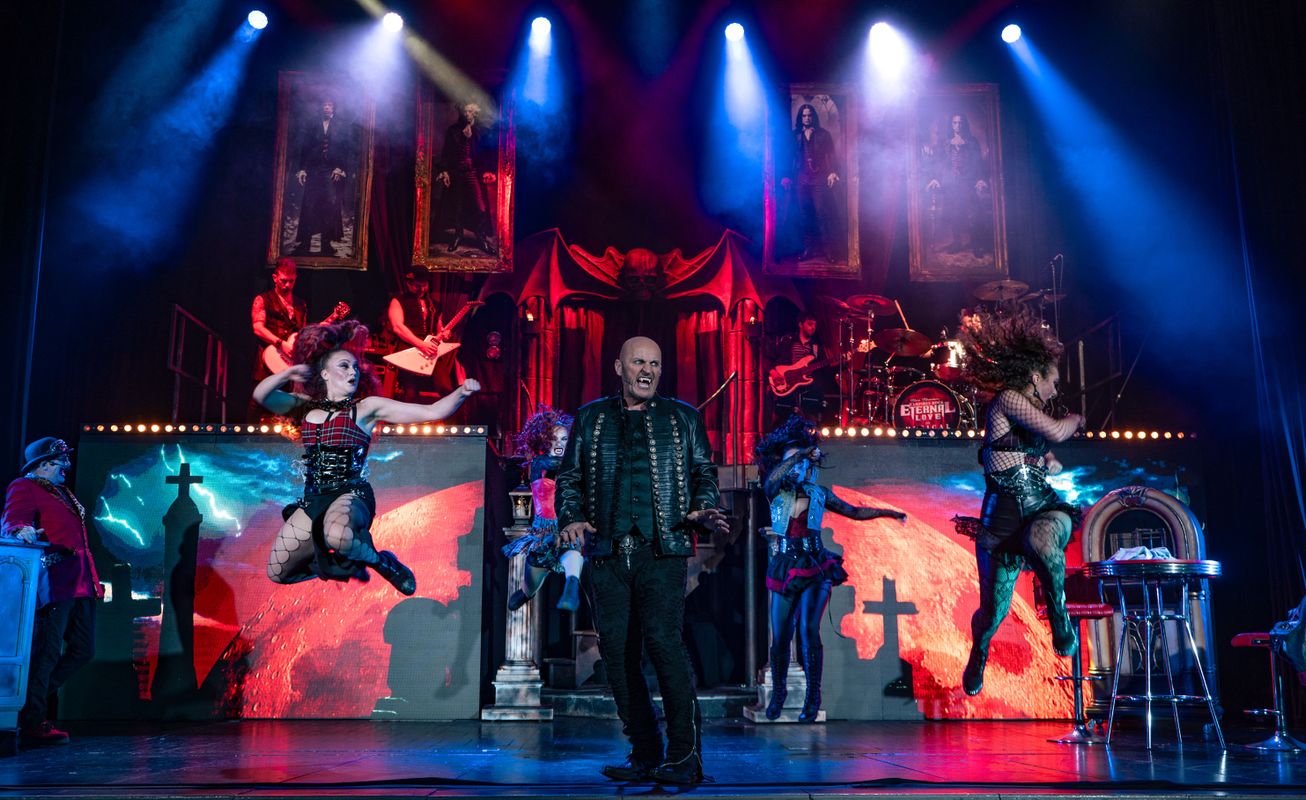 A person with pointy teeth looks menacing with others jumping around them.