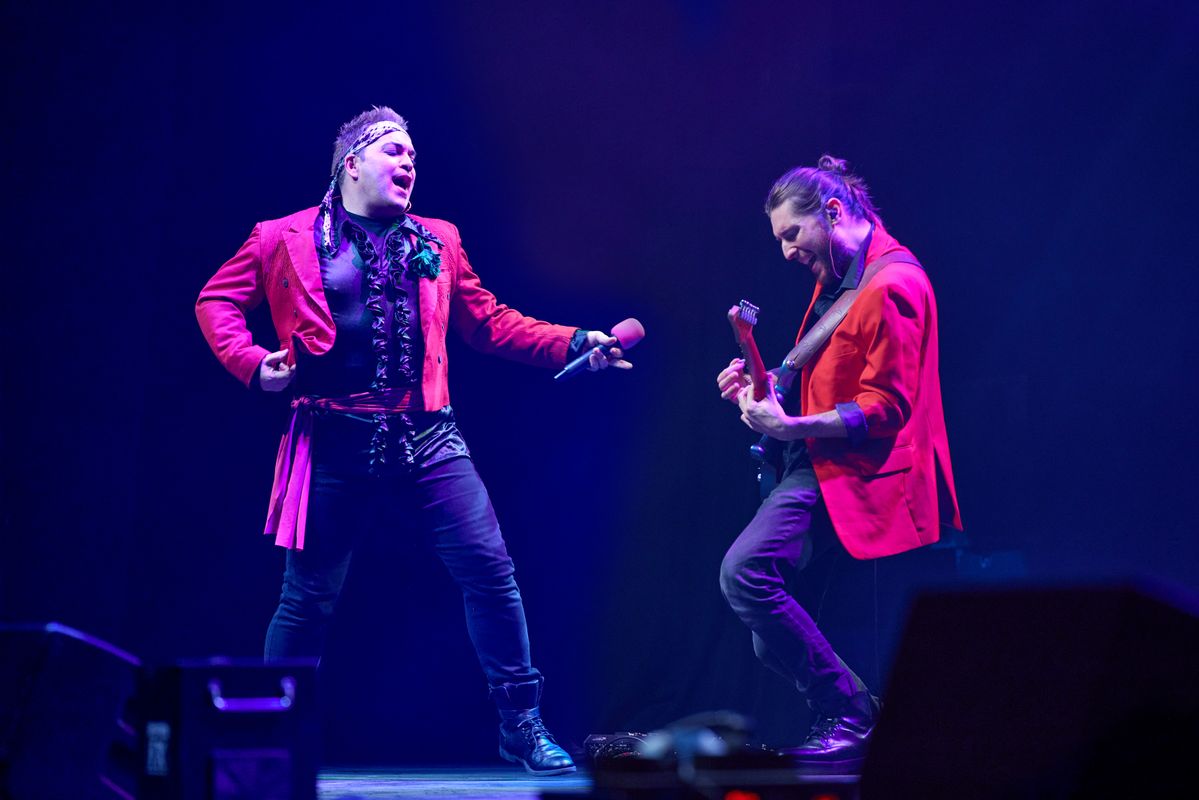 A person in a red jacket mimics the opposite guitarist. 