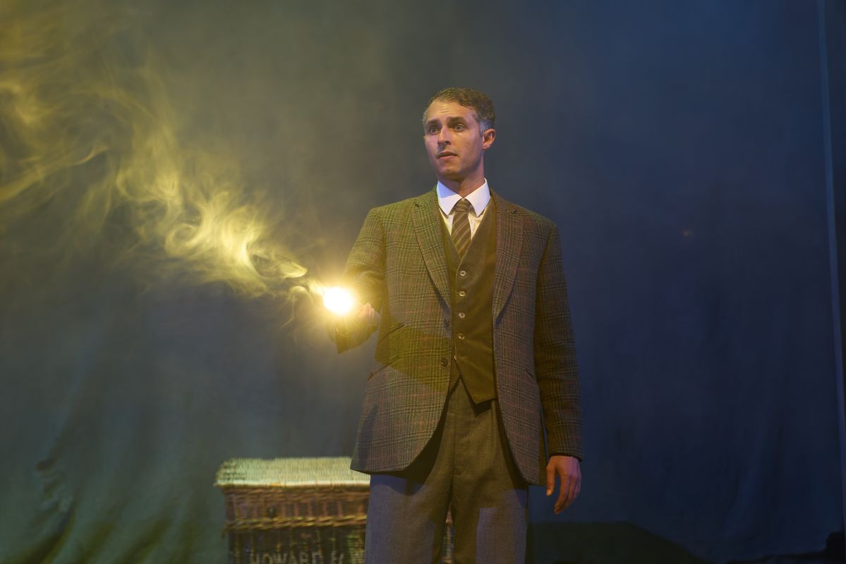 A person in a tweed suit holds a light.