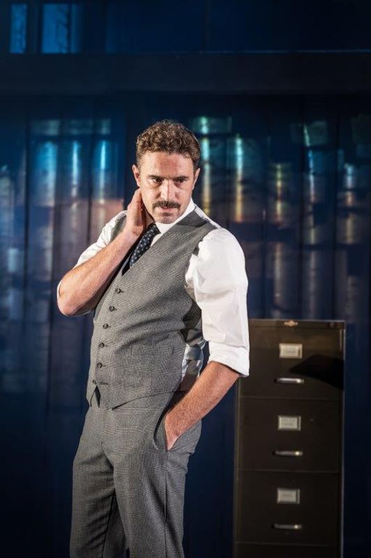 A man in a waistcoat and tie has his hand rested on his neck. He looks unsettled