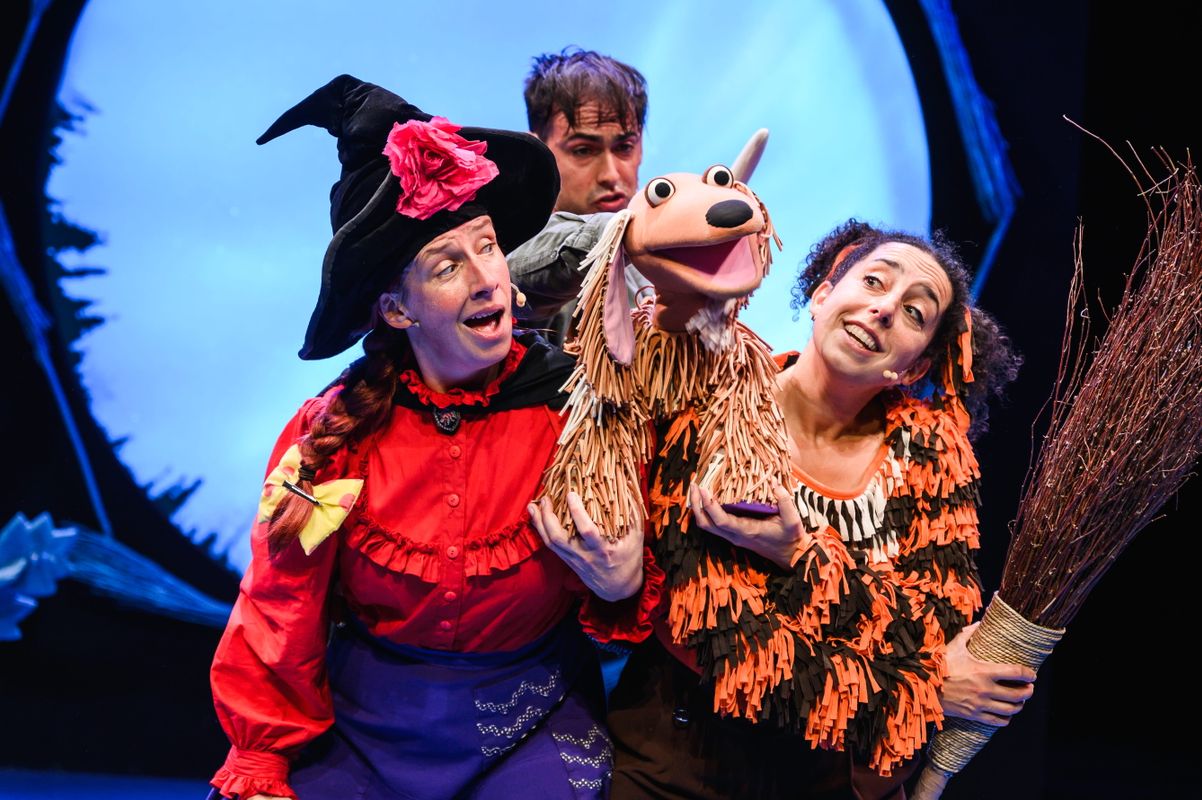 Three actors onstage with a dog puppet.
