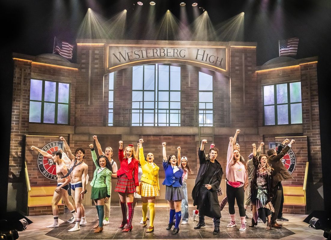 Stage performance at Westerberg High, featuring a diverse group of energetic actors in vibrant outfits, raising fists triumphantly, conveying excitement.