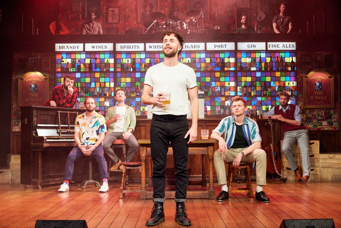 A person stands centre stage holding a beer.