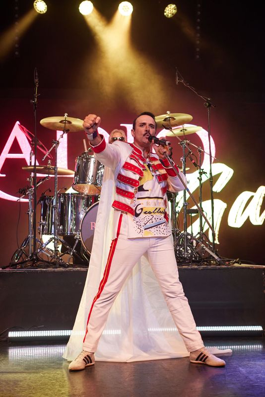 A man singing on stage and wearing a red and white jacket