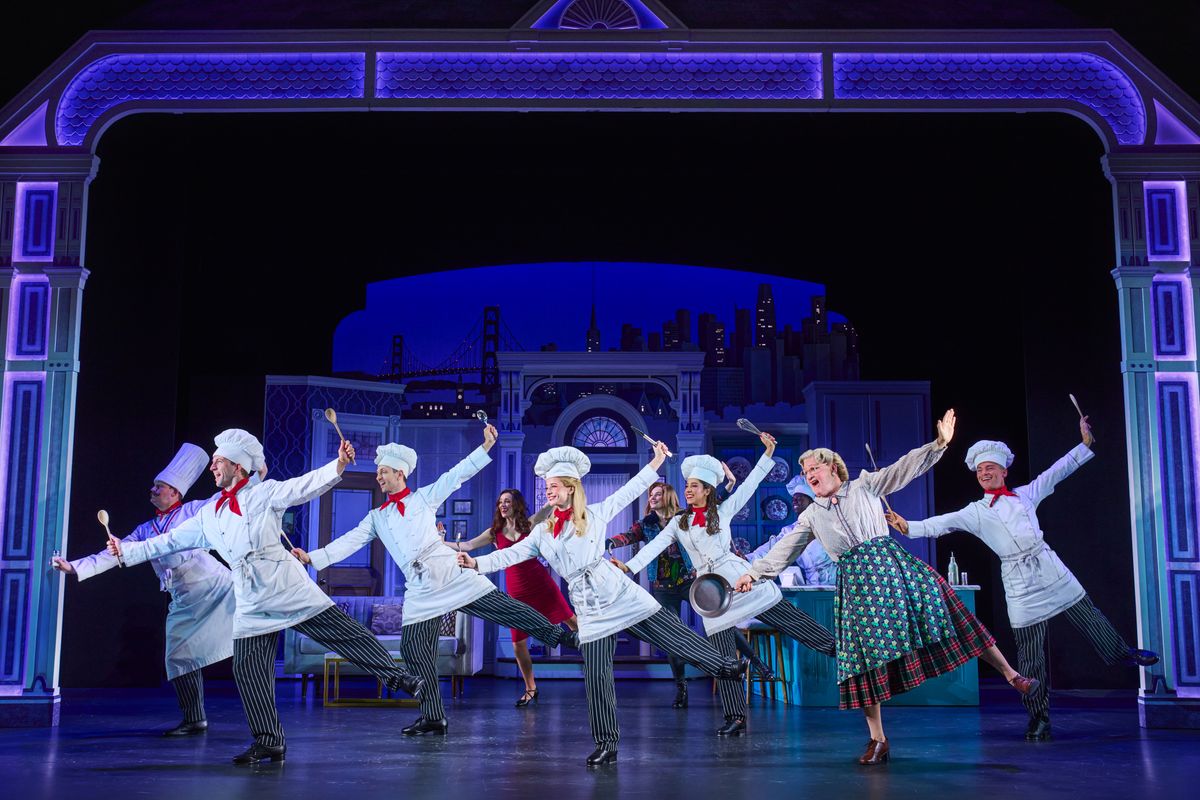Mrs Doubtfire dances on stage holding a frying pan surrounded by an ensemble dressed in chef costumes.