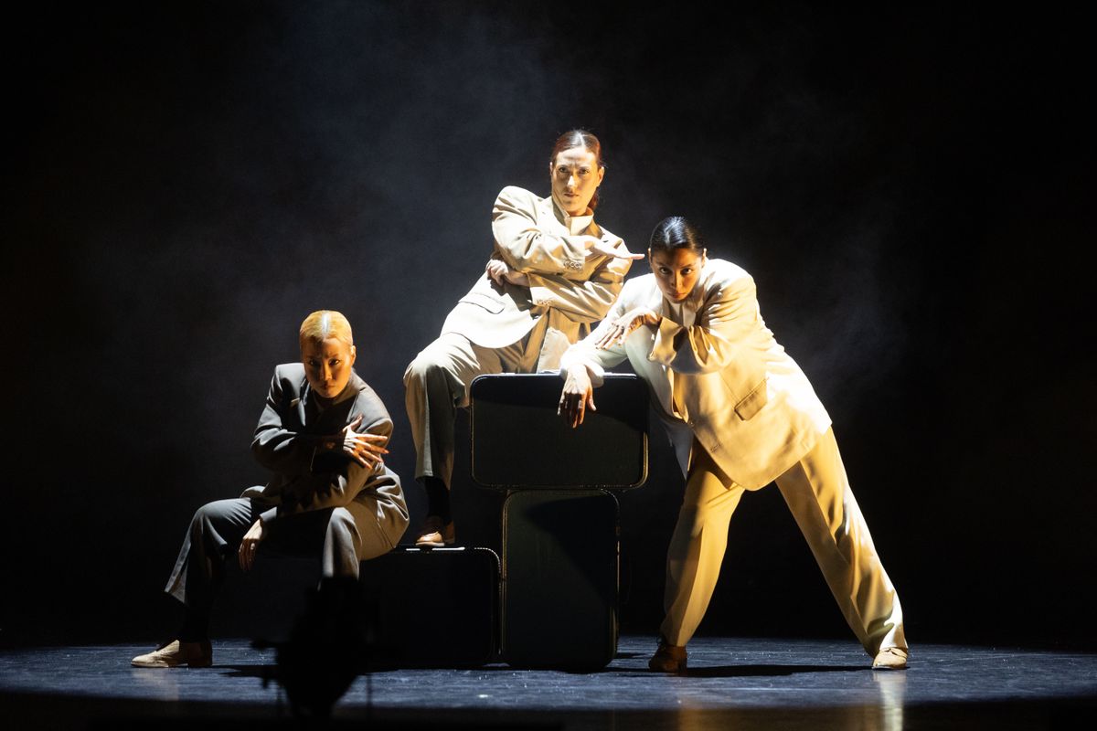 Three people dressed in neutral coloured suits lounge on three rectangle shaped boxes.