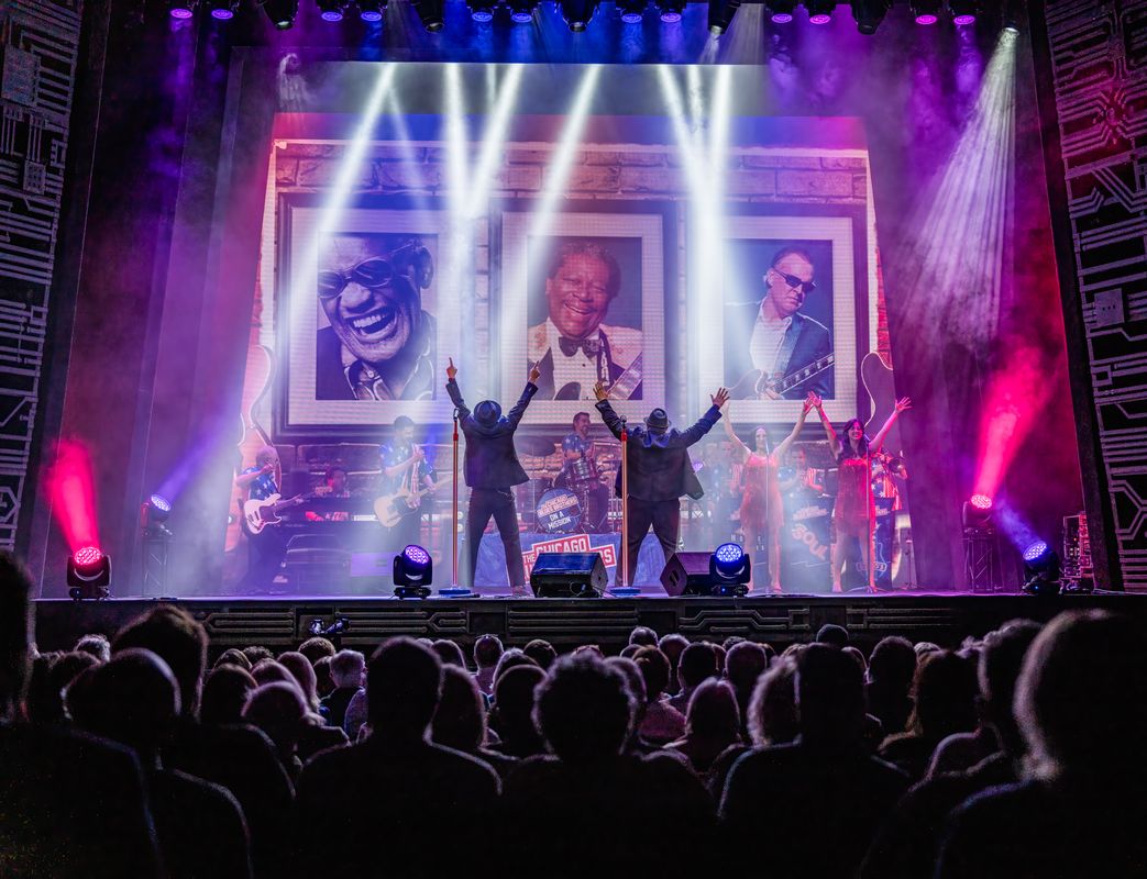 Two people dressed in suits and bowler hats reach out with their backs to the audience.