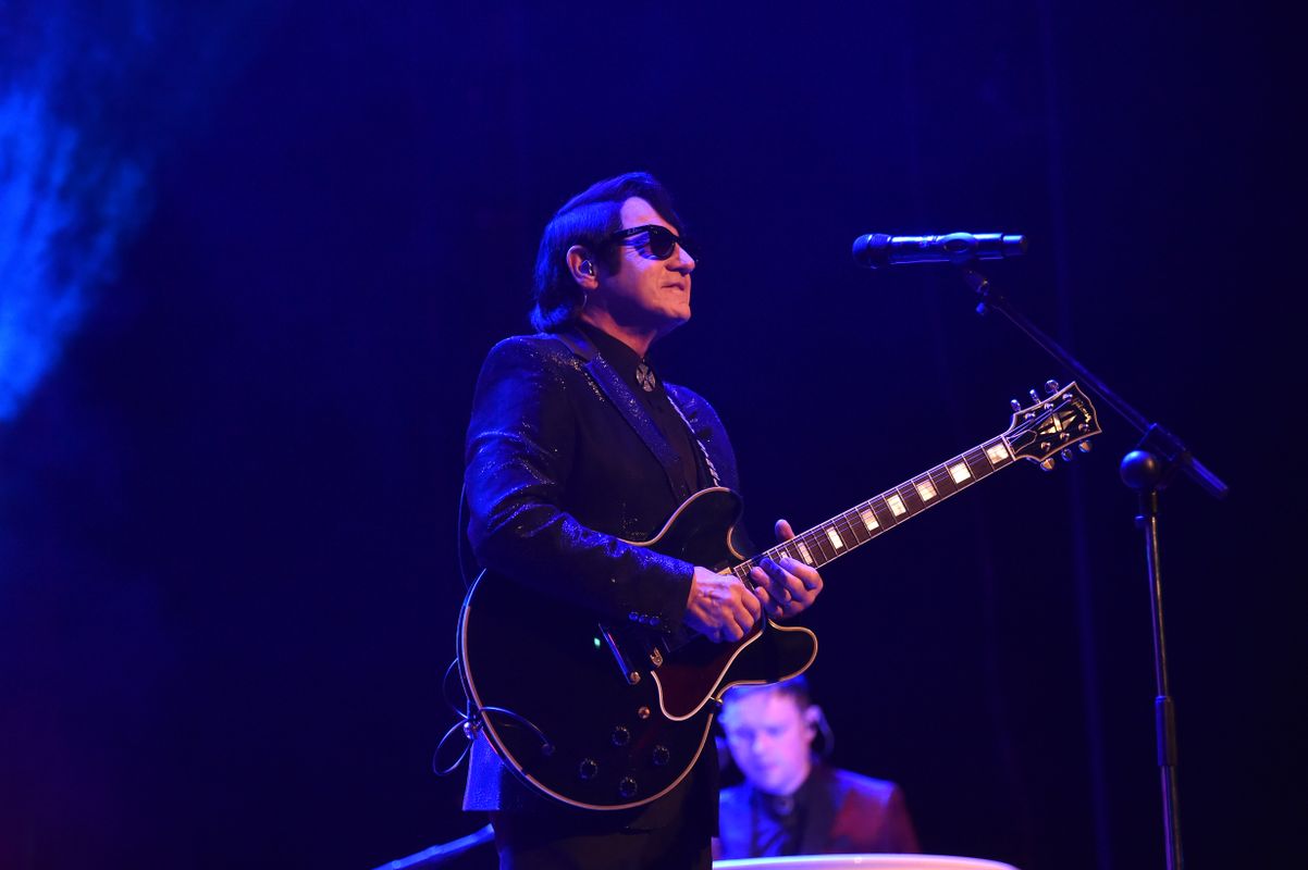 A person with a dark suit plays guitar.