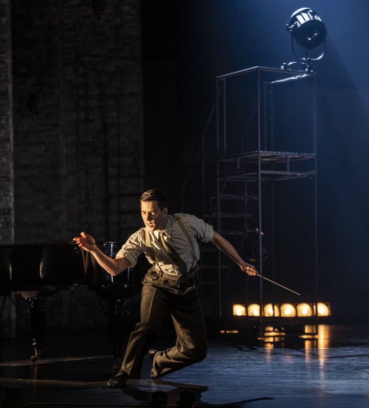 A person dances on stage with their left knee bent and right arm outstreched.