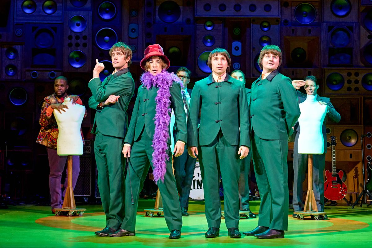 Dressed in green suits the band look out to the audience with the lead singer wearing a pink hat and purple feather boa.