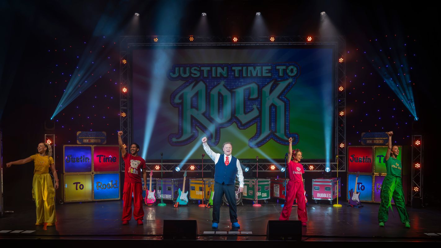 Justin and the ensemble stand on the stage with their right arms raised in a fist. 