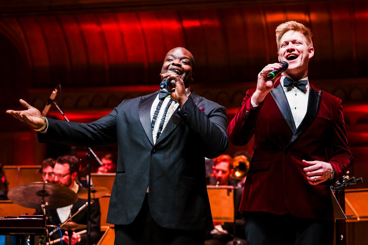 Two people dressed in suits sing on stage.