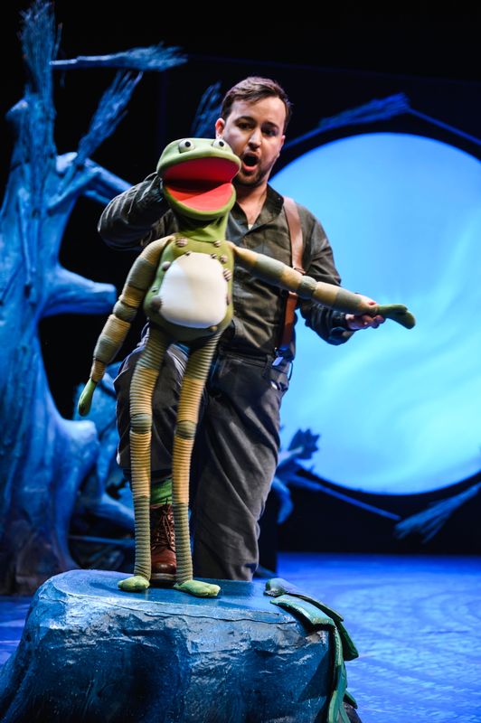 Actor holding a frog puppet onstage.