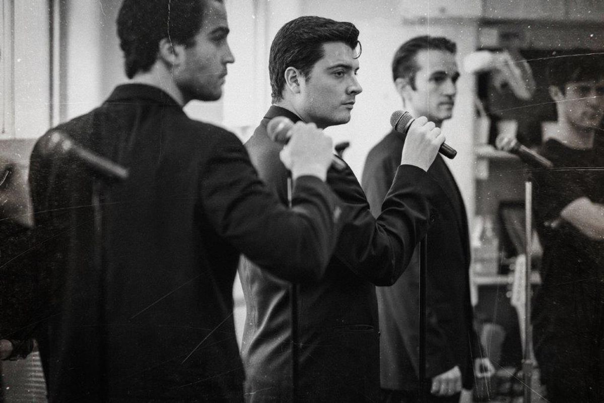 Black and white image of cats members rehearsing for Jersey boys. They are all wearing black and in a rehearsal studio