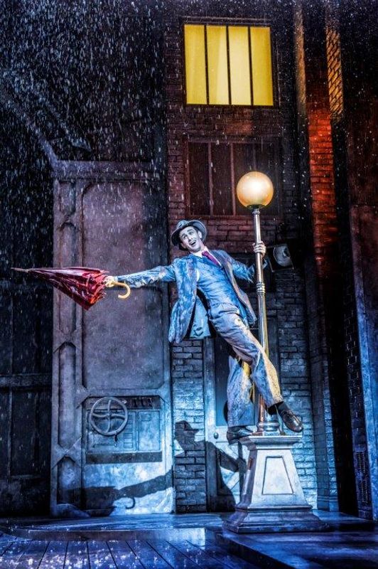 A man singing in the rain leaning from a lamp post and holding an umberella