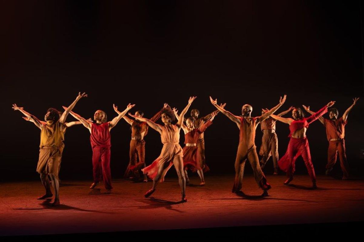 Group of dancers in orange and brown clothing with a soft spot light on them